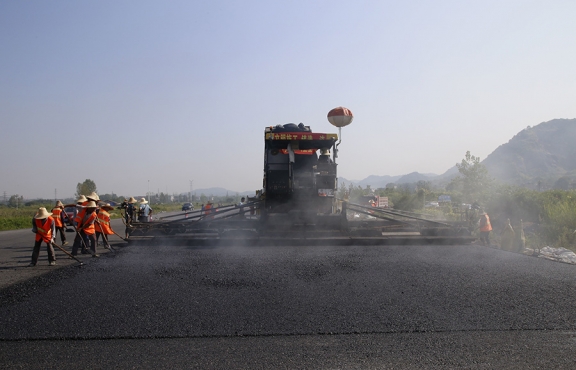 2019年8月，宜春經(jīng)開區(qū)S311路面攤鋪現(xiàn)場，工友們輔助路面兩側(cè)的分料、補(bǔ)窩等作業(yè)